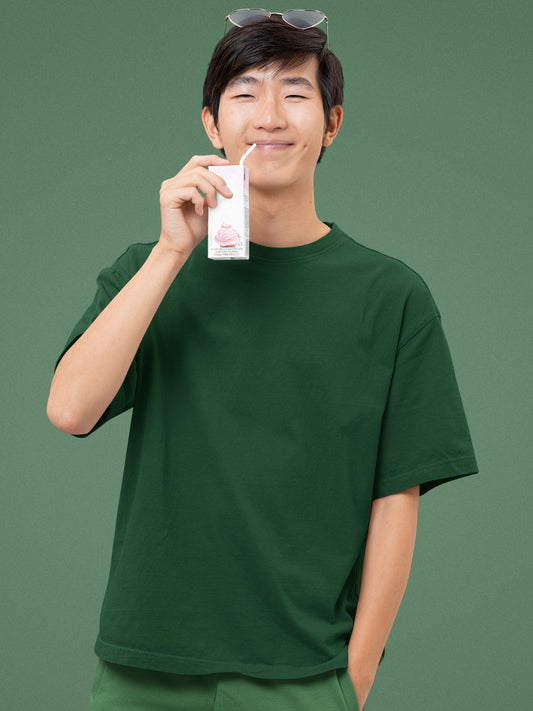In this delightful image, an Asian individual radiates joy with an infectious wide grin while sporting our Premium Heavyweight Bottle Green Oversized Tee. The rich green hue complements their cheerful demeanor. They add a playful touch to the scene by sipping from a milk carton, exuding a carefree and youthful spirit. This combination of a stylish tee and a carefree moment captures the essence of comfort and happiness.