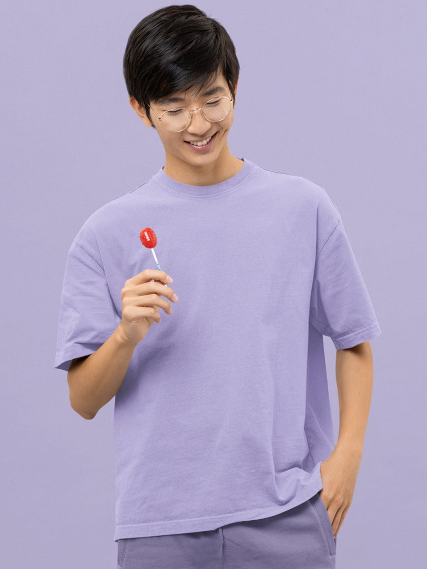 In this delightful image, a spectacled Asian gentleman radiates happiness and style. He confidently holds up a vibrant red lollipop, a playful contrast to his attire – our Premium Heavyweight Lavender Oversized Tee. The tee's soft lavender hue complements his cheerful demeanor, and his beaming smile reflects the perfect blend of comfort and fashion. This scene captures both his carefree spirit and fashionable individuality in a charming and memorable way.