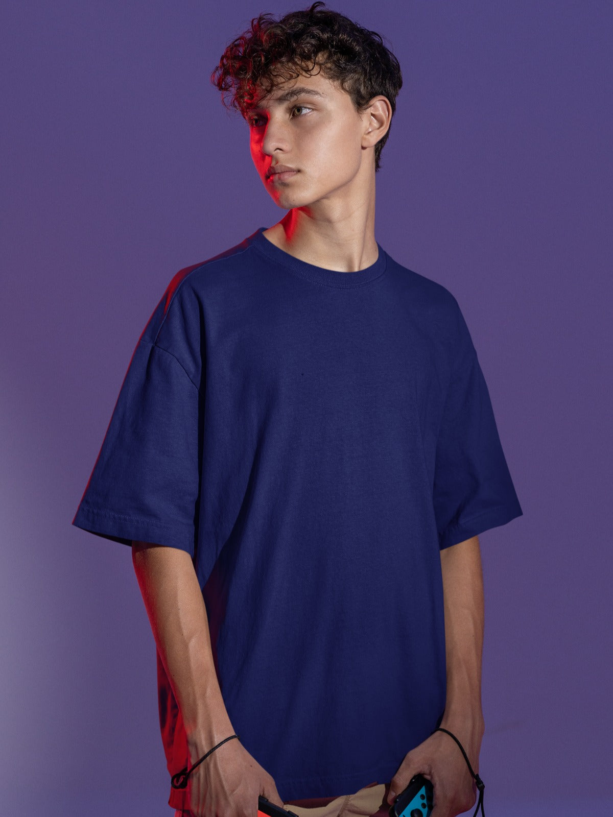 In this image, a lean and stylish white gentleman with a crown of brownish curly hair exudes a cool and enigmatic aura. He dons our Premium Heavyweight Navy Blue Oversized Tee, which drapes comfortably, emphasizing both comfort and timeless style. With a gaze turned sideways, his demeanor suggests a captivating blend of confidence and curiosity, perfectly encapsulating the tee's effortless charm and fashion-forward sensibility.