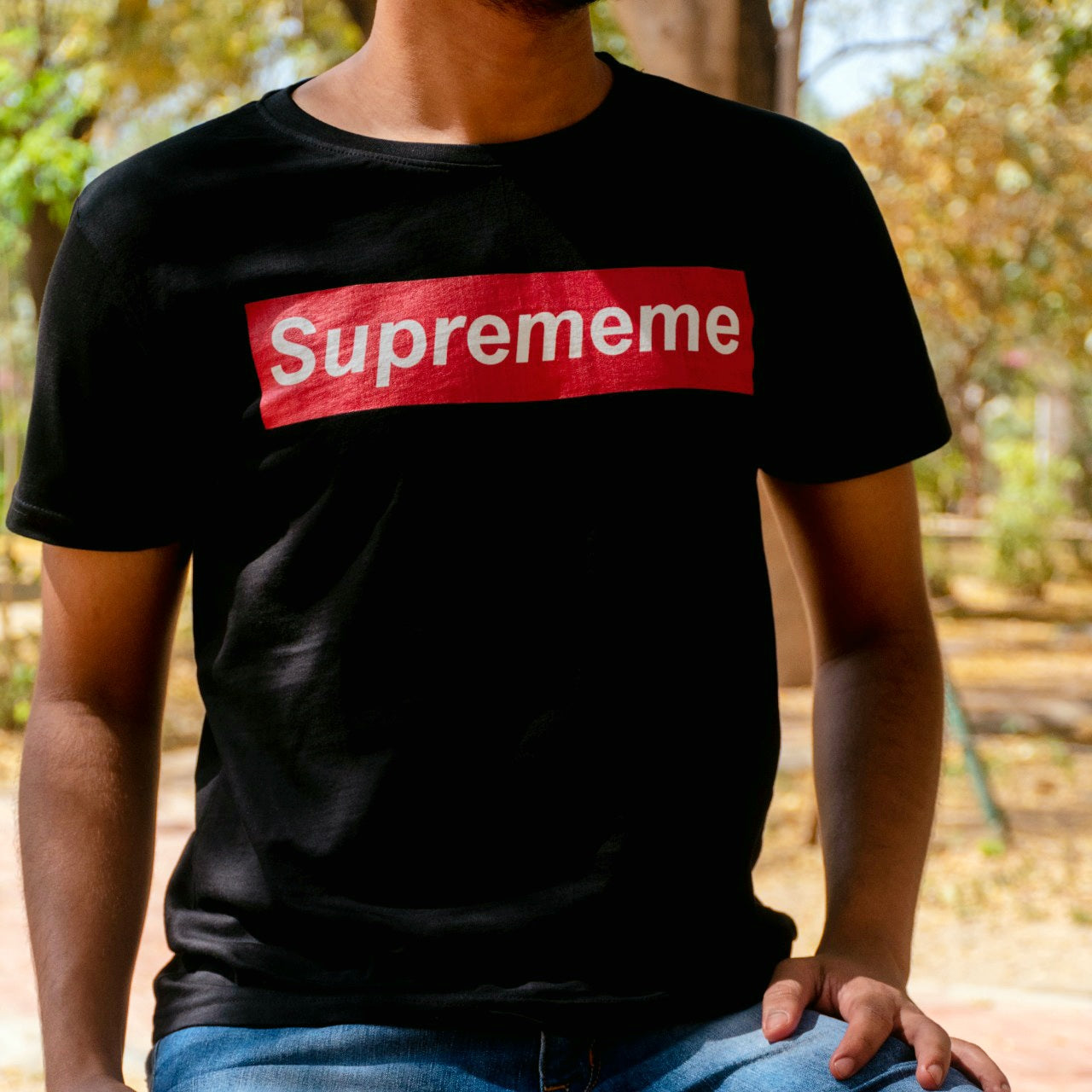 torso of man wearing a black tshirt with suprememe printed on it in red colour