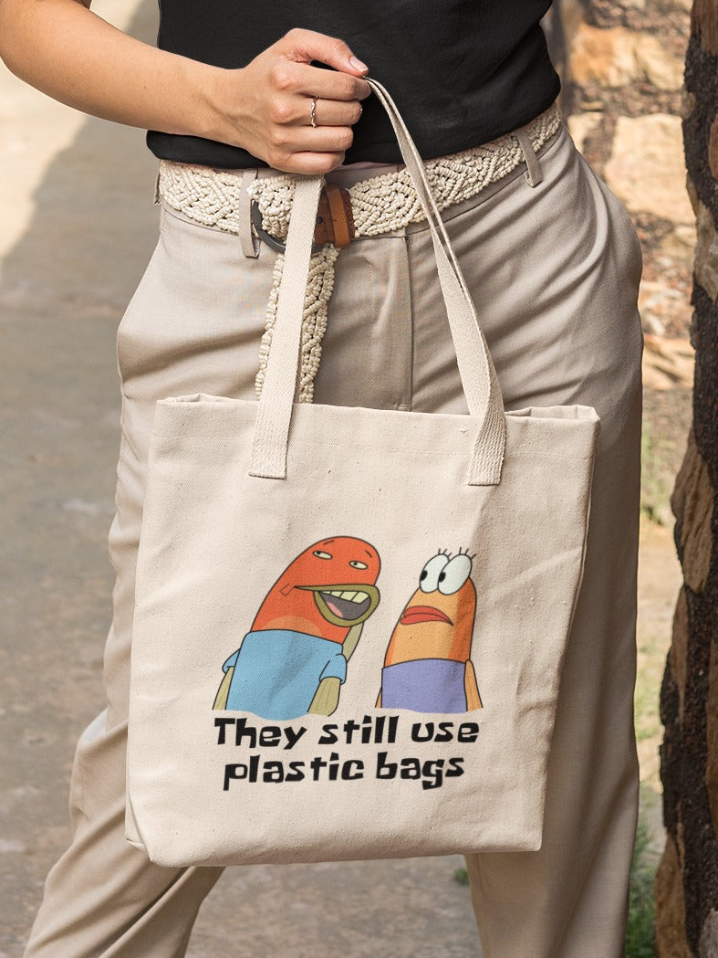 woman holding a canvas tote bag with fish characters from spongebob whispering to each other saying "they still use plastic bags" printed on it, environment memes
