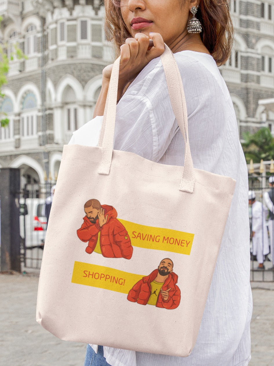 woman holding a canvas tote bag with hotline bling meme of drake selecting shopping against saving money printed on it, relatable memes