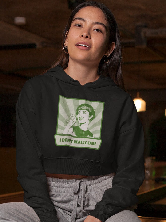 girl sitting on table top wearing a black crop hoodie with antique style illustration of woman talking on a phone saying I don't really care printed on it green monochrome, relatable sarcastic memes