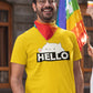 smiling man with spectacles wearing yellow tshirt with bongo cat saying hello written on it. The man has a rainbow pride cup in his hand and a rainbow lgbtq bandana. There is a rainbow pride flag in the background