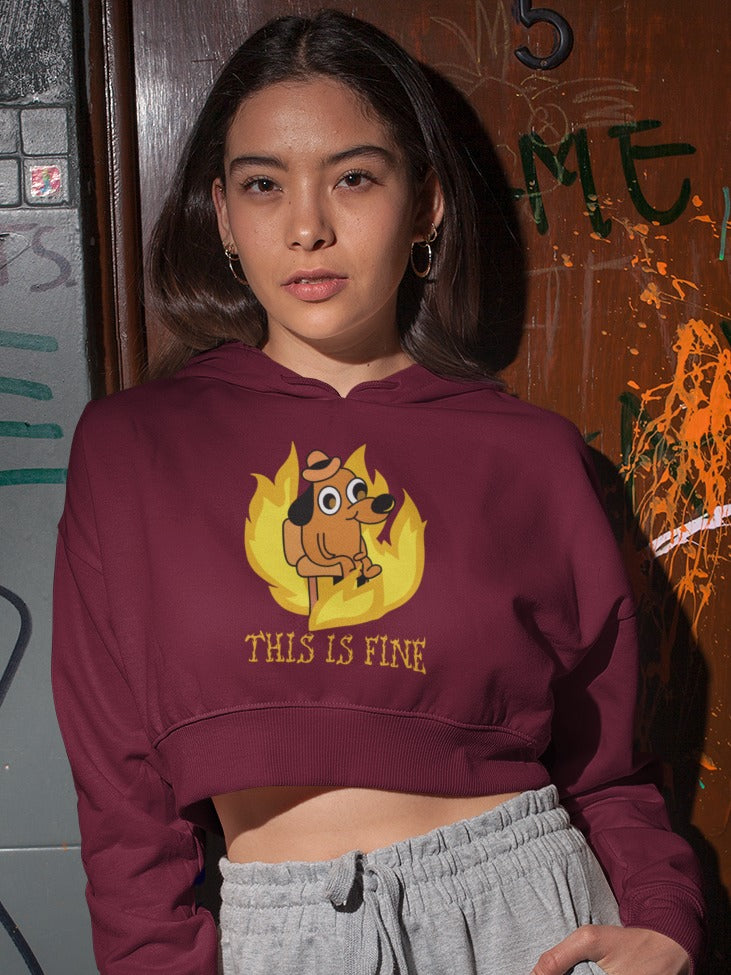 girl standing in front of a door wearing a maroon crop hoodie with a small dog sitting around a fire printed on it, "this is fine" in burning letters is printed below the dog