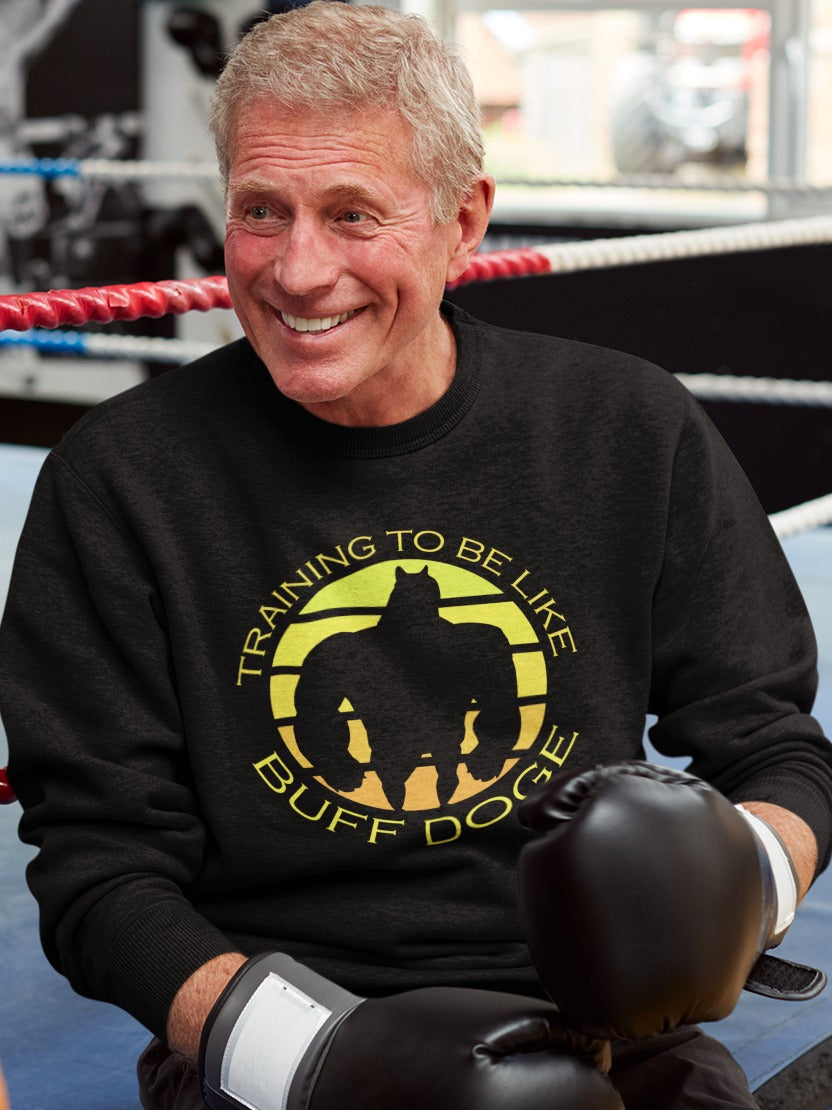 old man with boxing black boxing gloves sitting outside a boxing ring wearing a black sweatshirt with training to be like buff doge with silhouette of buffed up doge in the middle printed on it, gymming & training internet memes