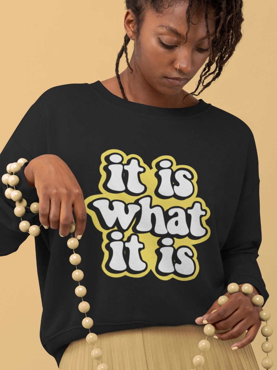brown girl with brown hair holding big wooden beads wearing a black sweatshirt with it is what it is printed on it, fun sayings, relatable sarcastic memes