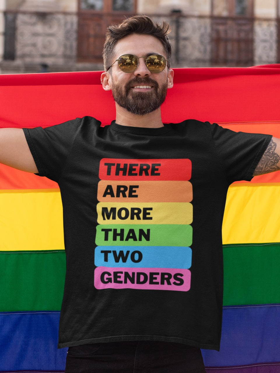 person wearing goggles and holding a rainbow flag is wearing a black tee with there are more than two genders written on it in rainbow palette